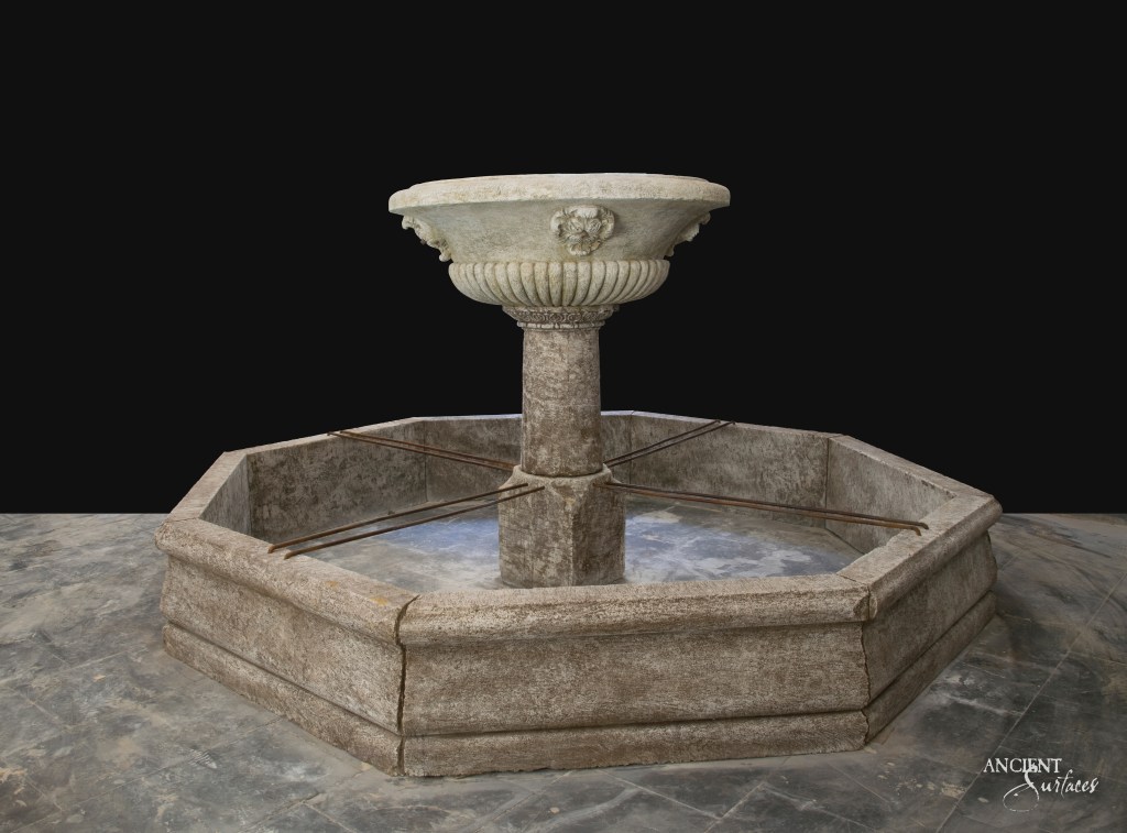 A rustic limestone pool fountain by Ancient Surfaces, its warm tones creating a cozy and inviting atmosphere in an outdoor living space.